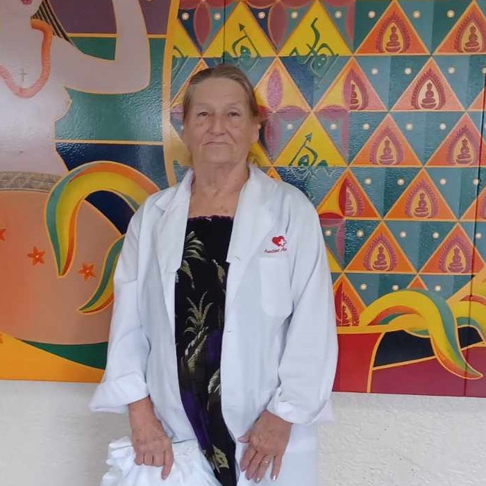 Auntie Dorella has a white lab coat with Auntie's Angels red logo on it, and is standing in front of a large mural of a woman.