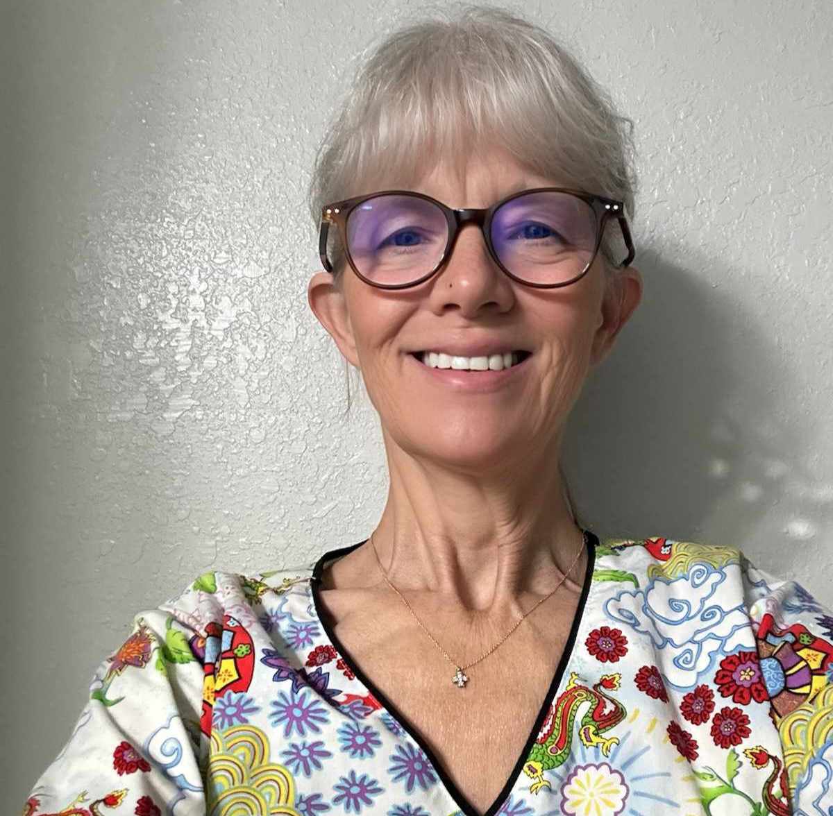 Lisa has a fair but tan complexion, glasses, platinum bangs, and a rainbow scrub top.